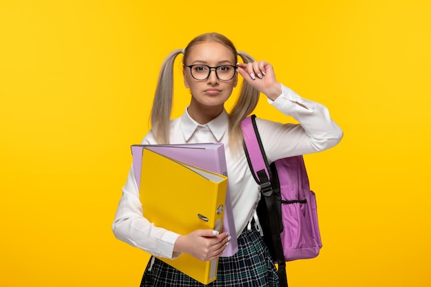 Menina loira do dia mundial do livro com rabos de cavalo usando mochila e segurando pastas