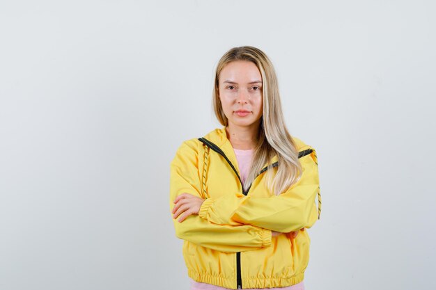 Menina loira em pé com os braços cruzados na jaqueta amarela e parecendo confiante.