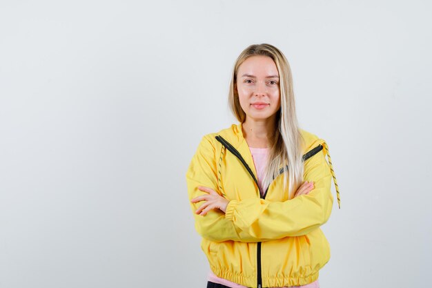 Menina loira em pé com os braços cruzados na jaqueta amarela e parecendo confiante.