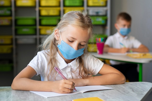 Menina loira escrevendo enquanto usava uma máscara médica