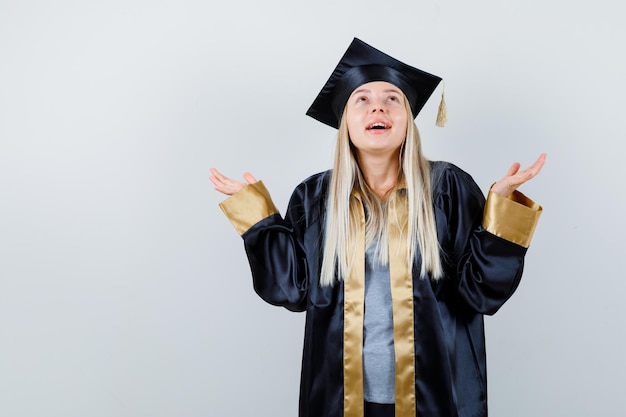 Menina loira esticando as mãos segurando algo e olhando para ele com vestido de formatura e boné e olhando focado