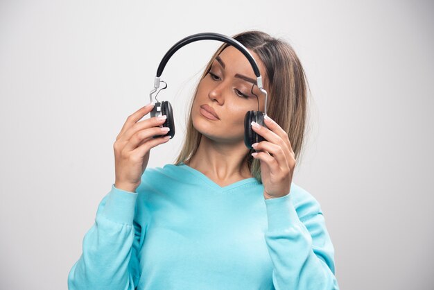 Menina loira no moletom azul segurando fones de ouvido e se prepara para usá-los para ouvir a música.