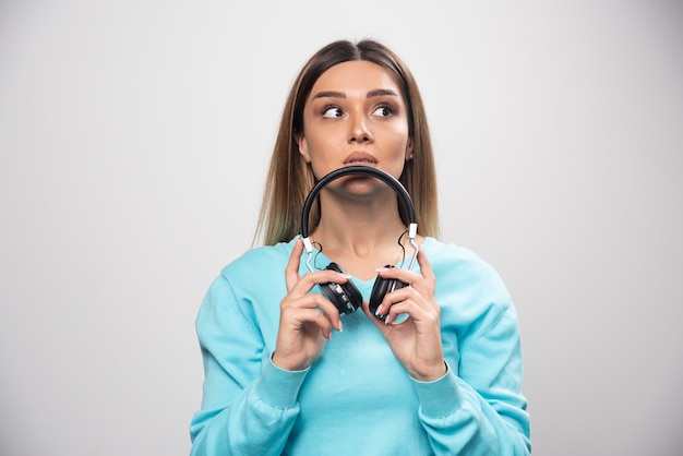 Menina loira no moletom azul segurando fones de ouvido e se prepara para usá-los para ouvir a música.