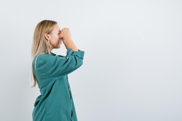 Menina loira olhando por entre os dedos na blusa verde e olhando com foco.