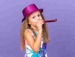 Foto grátis menina loira satisfeita com chapéu de festa violeta, soprando apito de festa e parecendo isolada na parede roxa com espaço de cópia