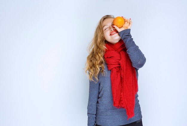 Menina loira segurando e demonstrando frutas laranja.