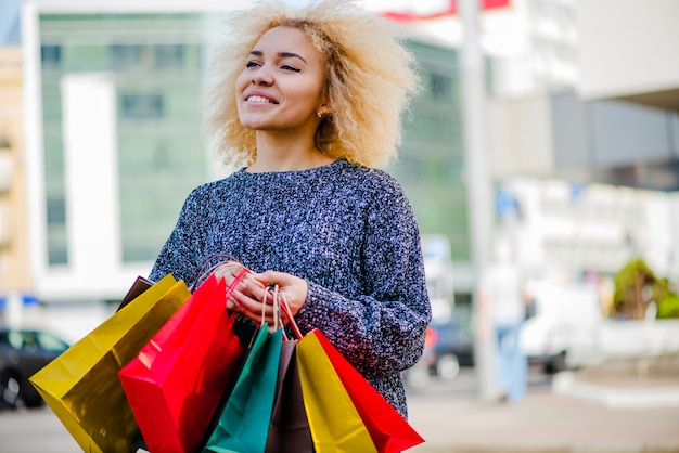 Menina loira segurando sacolas de compras sorrindo