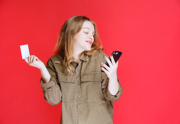 Menina loira segurando um cartão de visita e falando ao telefone.