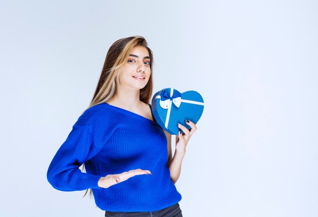 Menina loira segurando uma caixa de presente em forma de coração azul.