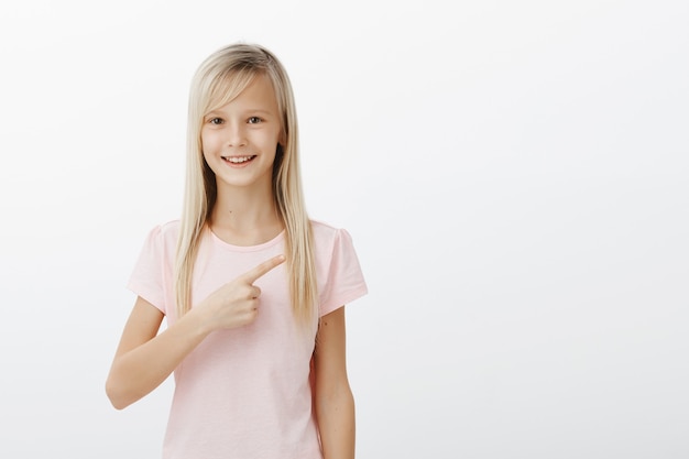 Menina loira sorridente e alegre apontando para o canto superior direito