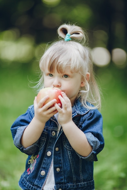 Menina loura pequena que morde uma maçã