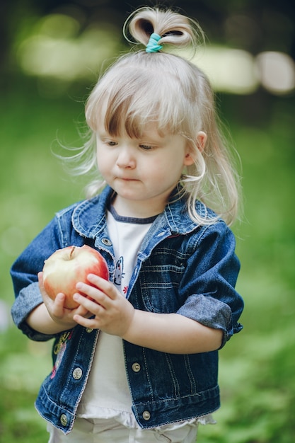 Menina loura pequena que prende uma maçã