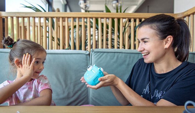 Menina, mãe e câmera digital de brinquedo para crianças para impressão instantânea de fotos.