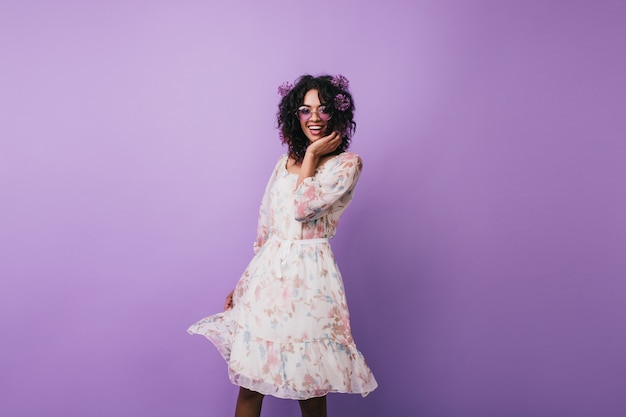 Menina magro com alliums no cabelo dançando feliz. Agradável jovem africana em vestido vintage posando.