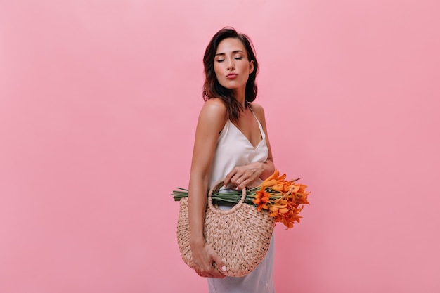 Menina mandando beijo e segurando uma bolsa com flores em fundo rosa