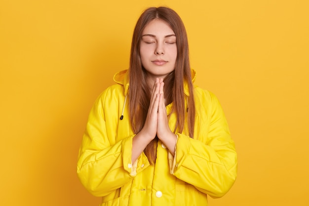 Menina meditando ou rezando na parede amarela