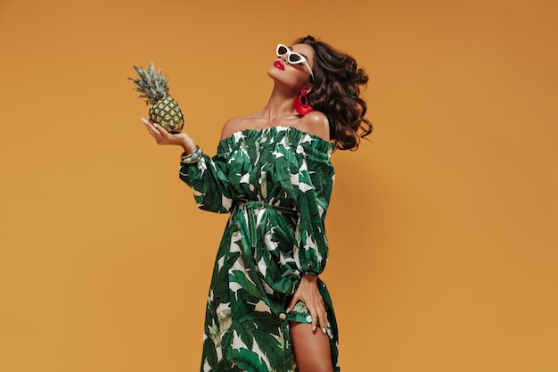 Menina moderna de cabelo encaracolado com lábios grandes vermelhos brilhantes e brincos incomuns em um vestido de verão verde e branco elegante e óculos de sol