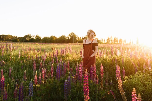 Menina moderna do moderno que anda no campo do wildflower no por do sol.