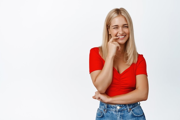 Menina moderna elegante pisca sorrisos e ri flirty fica em roupas de verão contra fundo branco