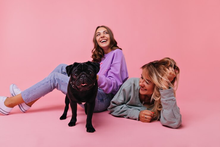 Foto grátis menina morena animada sentada no chão com o bulldog negro. retrato interno de duas amigas se divertindo com um lindo animal de estimação.