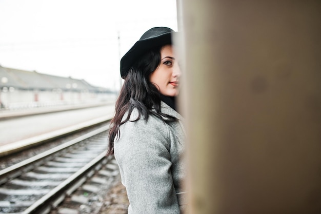 Menina morena de casaco cinza com chapéu na estação ferroviária