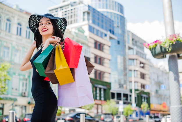 Menina morena de pé na rua segurando bolsas