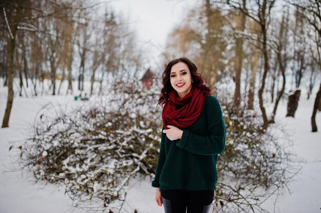 Menina morena de suéter verde e lenço vermelho ao ar livre na noite de inverno