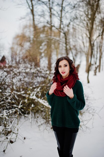 Menina morena de suéter verde e lenço vermelho ao ar livre na noite de inverno