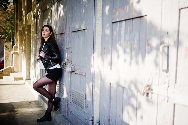 Menina morena elegante usa jaqueta de couro e shorts posando na rua