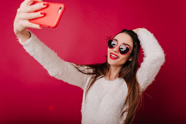 Menina morena em êxtase brincando com seu cabelo enquanto tira uma foto