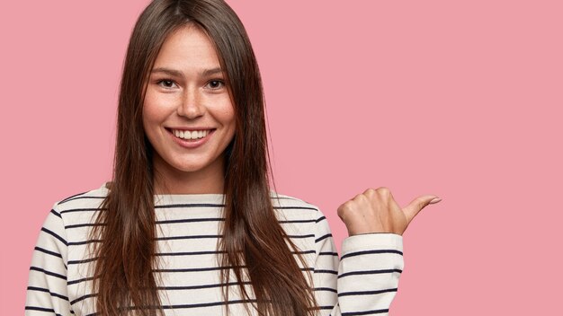 Menina morena feliz com sorriso charmoso e atraente, apontando para o lado