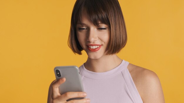 Menina morena muito sorridente conversando com amigos online em smartphone isolado em fundo colorido