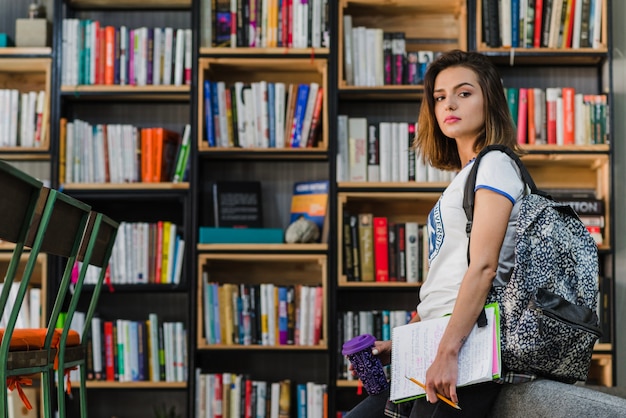 Menina morena segurando blocos notas copo sentado