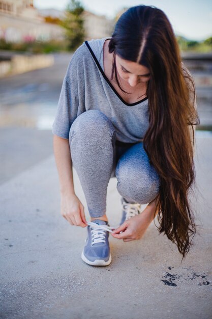 Menina morena sentada, amarrando sapatos