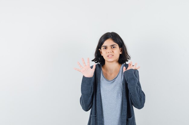 Menina mostrando as palmas das mãos em gesto de rendição na t-shirt, jaqueta e parecendo confusa.