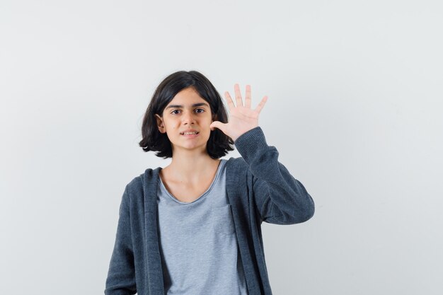 Menina mostrando cinco dedos na camiseta, jaqueta e parecendo confiante.