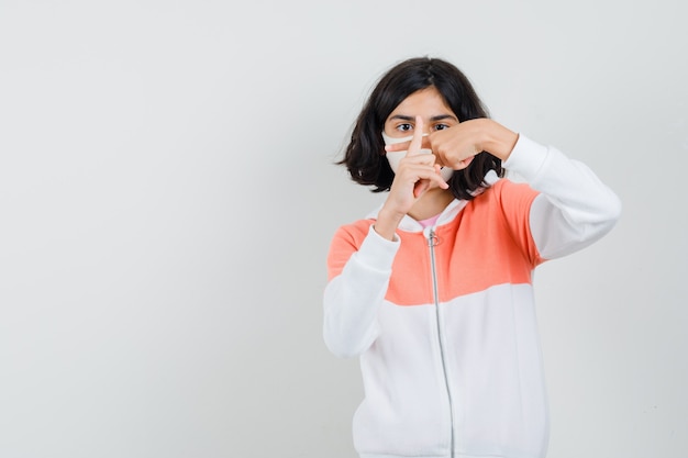 Menina mostrando dedos cruzados formando um x na jaqueta, máscara