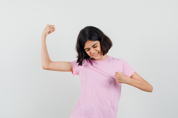 Menina mostrando gesto de vencedor em t-shirt rosa e parecendo com sorte. vista frontal.