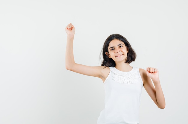 Menina mostrando gesto de vencedor na blusa branca e parecendo feliz. vista frontal.