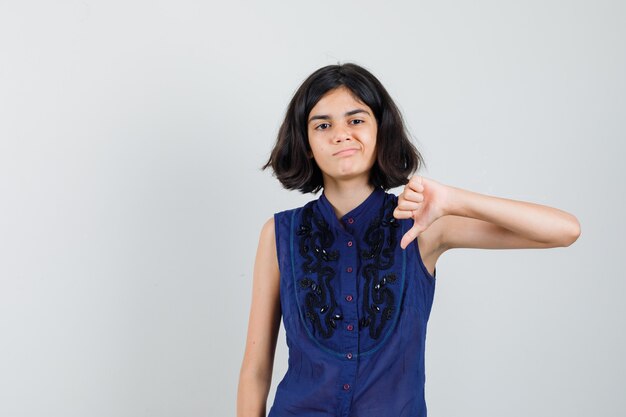 Menina mostrando o polegar para baixo na blusa azul e parecendo insatisfeita.