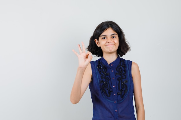 Menina mostrando um gesto ok na blusa azul e parecendo satisfeito.