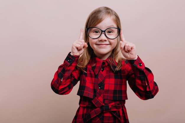 Foto grátis menina muito esperta em pé sobre uma parede bege segurando o dedo grande com um sorriso