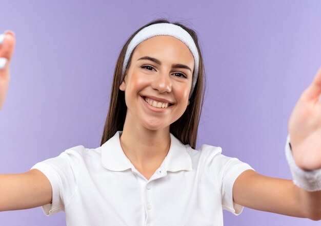 Menina muito esportiva sorridente usando bandana e pulseira, estendendo as mãos isoladas no espaço roxo