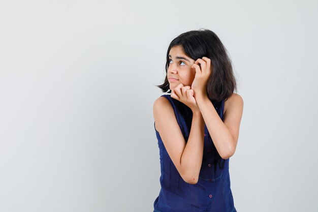 Menina na blusa azul, olhando para cima e parecendo curiosa.