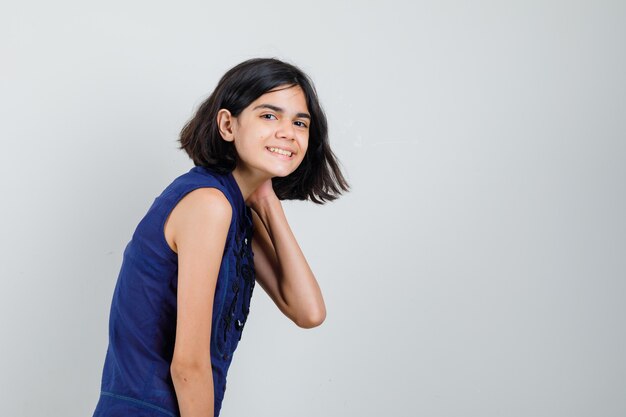 Menina na blusa azul, posando com a mão no pescoço e olhando otimista.