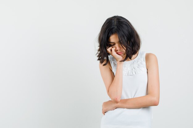 Menina na blusa branca em pé em pose de pensamento e olhando triste, vista frontal.