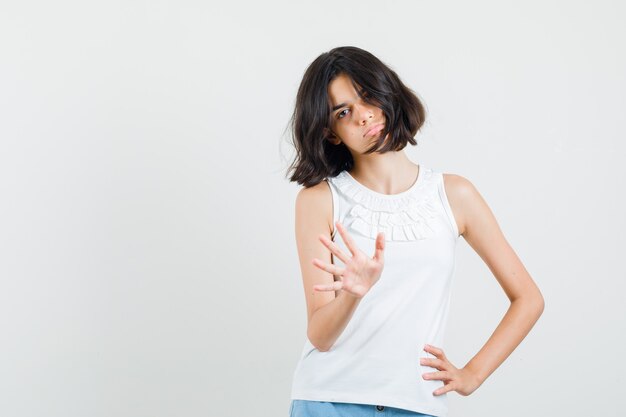 Menina na blusa branca, shorts mostrando gesto de parada e parecendo cansada, vista frontal.