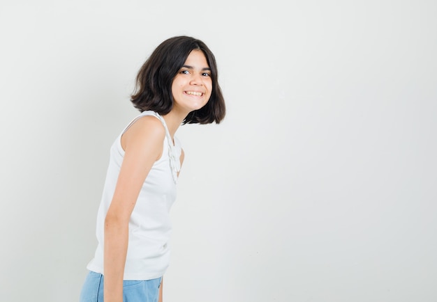 Menina na blusa branca, shorts, olhando para a frente e parecendo alegre.