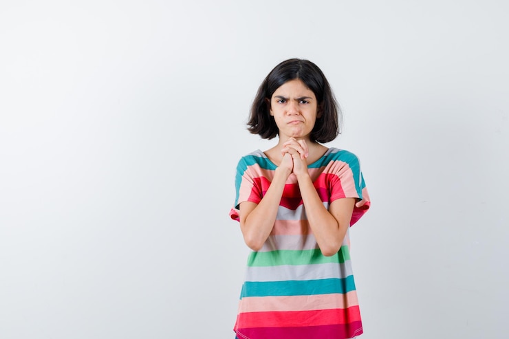Foto grátis menina na camiseta, apertando as mãos, fazendo caretas e parecendo descontente, vista frontal.