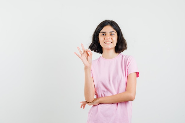 Menina na camiseta rosa, fazendo o gesto de ok e parecendo feliz, vista frontal.